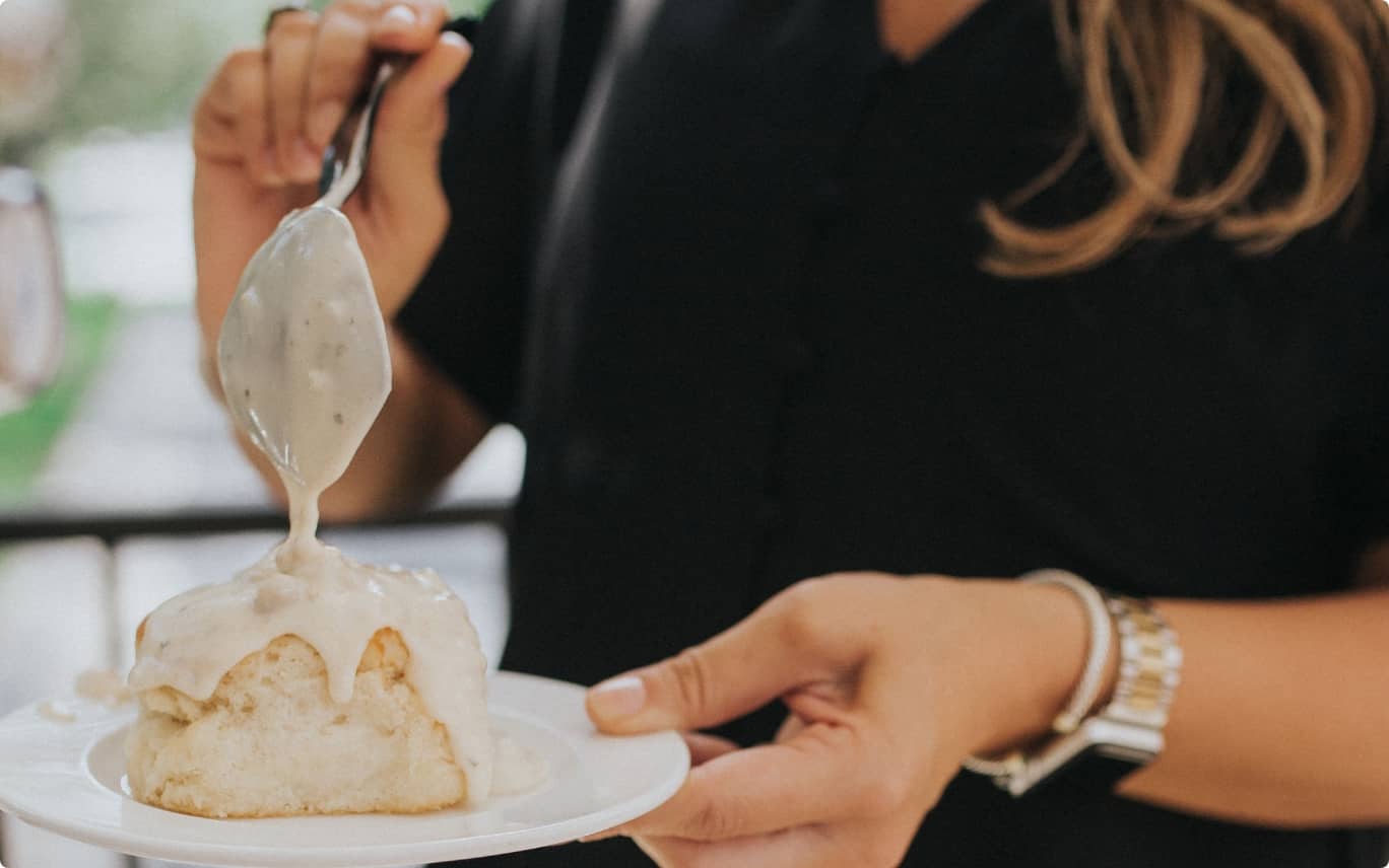 person with black shirt spooning gravy over a biscuit